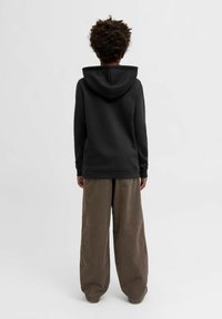 Felpa nera con cappuccio realizzata in tessuto morbido, abbinata a pantaloni larghi beige chiaro. Finitura texturizzata su entrambi i capi.