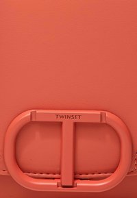 Borsa in pelle corallo con una prominente fibbia rettangolare recante il logo "TWINSET". Texture liscia con dettagli di cucitura minimi.