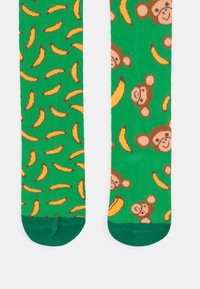 Grønne sokker med et leken mønster av tegneserier.aper og bananer, laget av mykt strikket materiale med forsterket tå.