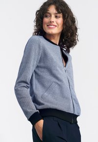 Niebieska bomberka w wzór jodełki z zamkiem z przodu, czarnym prążkowanym dekoltem i mankietami. Posiada boczne kieszenie i textured finish.