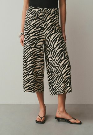 Woman wearing black and white zebra-print wide-leg cropped pants with black heeled sandals against a plain background.