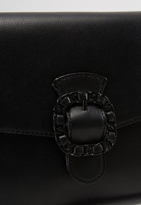 Pochette en cuir noir avec une finition texturée, dotée d'un accent en chaîne et d'un rabat rectangulaire.