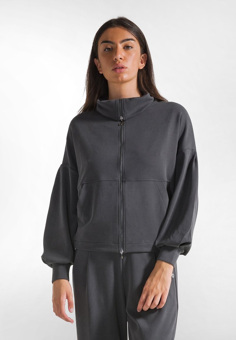 Giacca zip-up grigio scuro con colletto alto, maniche lunghe a palloncino e tessuto testurizzato. Presenta una cerniera e cuciture lungo il torso.