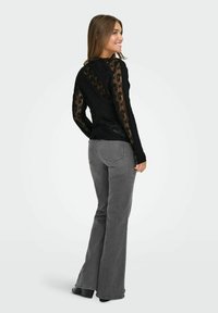 Black lace top with long sleeves, textured pattern, paired with gray flared jeans. Smooth fabric with a fitted design and round neckline.