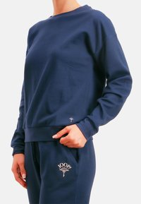 Granatowa bluza z długimi rękawami i okrągłym dekoltem. Z małym logo u dołu. Miękka tkanina o luźnym kroju.