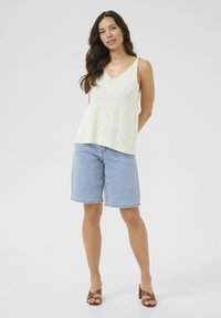 Light yellow sleeveless top with a V-neck, paired with light blue denim shorts. Brown strappy block heels complete the outfit.