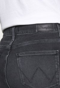 Černé džíny z denimu s koženou nášivkou Wrangler na zadním pásu a výrazným šitím zadních kapes ve výrazném tvaru "W".