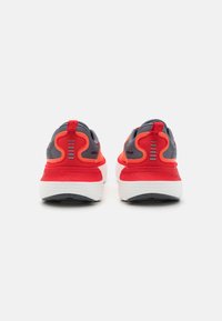 Chaussures de sport rouge et grise avec dessus en maille, col rembourré et semelle intermédiaire blanche. Présente un design unique au niveau du talon et des accents réfléchissants.