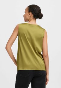 Top sin mangas color verde oliva con una textura suave y brillante. Corte holgado con escote redondo y aberturas laterales, combinado con pantalones oscuros.