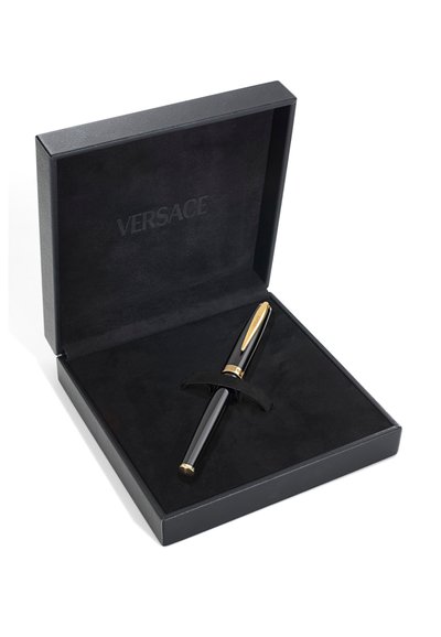 Bolígrafo de lujo negro y dorado reposando en una caja abierta forrada de terciopelo negro con "Versace" grabado en el interior de la tapa.
