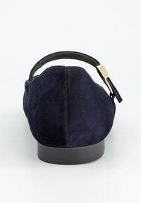 Zapato plano de ante azul marino con tacón redondeado, suela negra y tira delgada ajustable con hebilla dorada en la parte posterior.