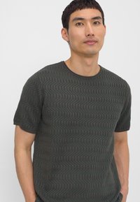 Mørkegrøn kortærmet t-shirt med et struktureret hørfiskemønster, der har en rund halsudskæring og en let tilpasset pasform.