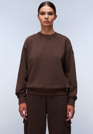 Bruine sweatshirt met een ronde hals, ribbelboorden en -zoom. Heeft een losse pasvorm en een zachte textuur, gecombineerd met bijpassende bruine broeken.