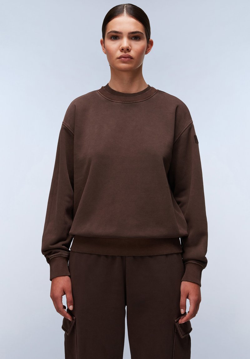 Bruine sweatshirt met een ronde hals, ribbelboorden en -zoom. Heeft een losse pasvorm en een zachte textuur, gecombineerd met bijpassende bruine broeken.