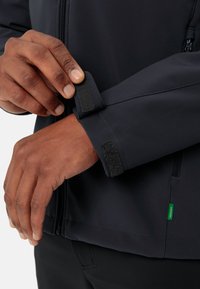 Granatowa kurtka typu softshell posiada regulację mankietów na rzepy, zamek błyskawiczny oraz zielony detal w okolicy dołu. Materiał wydaje się gładki i trwały.