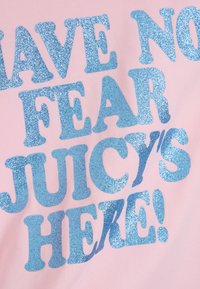 Tissu rose avec un grand texte étincelant bleu clair disant "N'AIE PAS PEUR, JUICY EST LÀ !" Le texte a une texture scintillante.