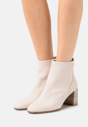 Bottines en cuir beige à bout pointu et au design courbé ; elles présentent un talon bloc texturé avec une apparence en bois et un accent métallique.
