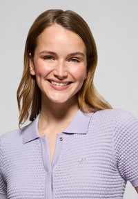 Lila poloshirt met een gestructureerd breisel, korte mouwen en een knoopsluiting met een klein geborduurd logo op de borst.