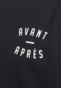 Black fabric t-shirt featuring white text that reads "AVANT - APRÉS," with a simple, clean design and no additional graphics or patterns.