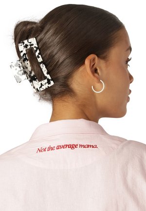 Klarer Acrylhaargeclips mit schwarz-weißen Sprenkeln, der einen Haarknoten sichert. Rosa Hemd mit rotem sticktem Text "Nicht die durchschnittliche Mama" am Kragen.