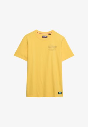 T-shirt gialla a maniche corte con scollo tondo, con piccolo logo "Superdry Outfitters Co." sul petto e toppa rettangolare vicino all'orlo inferiore.