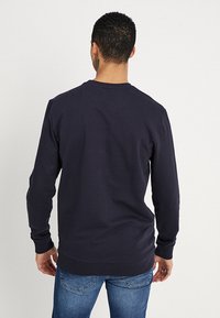 Granatowy sweatshirt wykonany z bawełny, z długimi rękawami i okrągłym dekoltem. Gładka struktura z prążkowanymi mankietami i dołem. Prosty design.