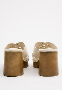 Zuecos beige de espalda abierta con correas anchas, que presentan un acabado suave, remaches decorativos y un tacón grueso marrón.