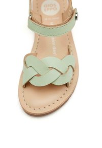 Sandalia de cuero verde menta con un diseño superior trenzado, correa ajustable en el tobillo y plantilla de cuero marrón claro con detalles de costura.