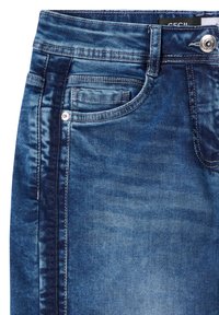 Gros plan sur un jean en denim bleu avec poche avant, petite poche, passants de ceinture et fermeture par bouton métallique.
