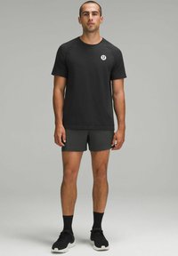 T-shirt de sport noir avec une texture subtile et des manches courtes, associé à un short sombre et des chaussures de sport noires avec des semelles blanches.