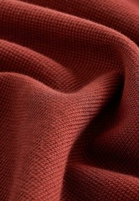Teksturomat, rødbrun stof med et hævet gittermønster, der viser bløde, vævede fibre. Materialet fremstår hyggeligt og fleksibelt.