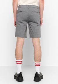 Gray tailored shorts with a straight cut, featuring back pockets and a smooth texture. Worn with red-striped white socks and black chunky shoes.