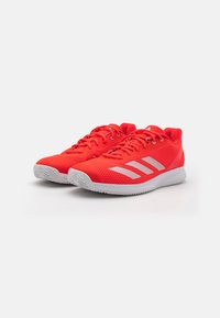 Adidași roșii de sport cu partea superioară din plasă, având accente de dungi albe și o talpă texturată. Vârf rotunjit și design cu șireturi.