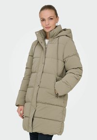 Beige polstret parka med hætte, der har lynlåslukning foran, sidelommer og quiltet tekstur. Mellemlang model for varme.