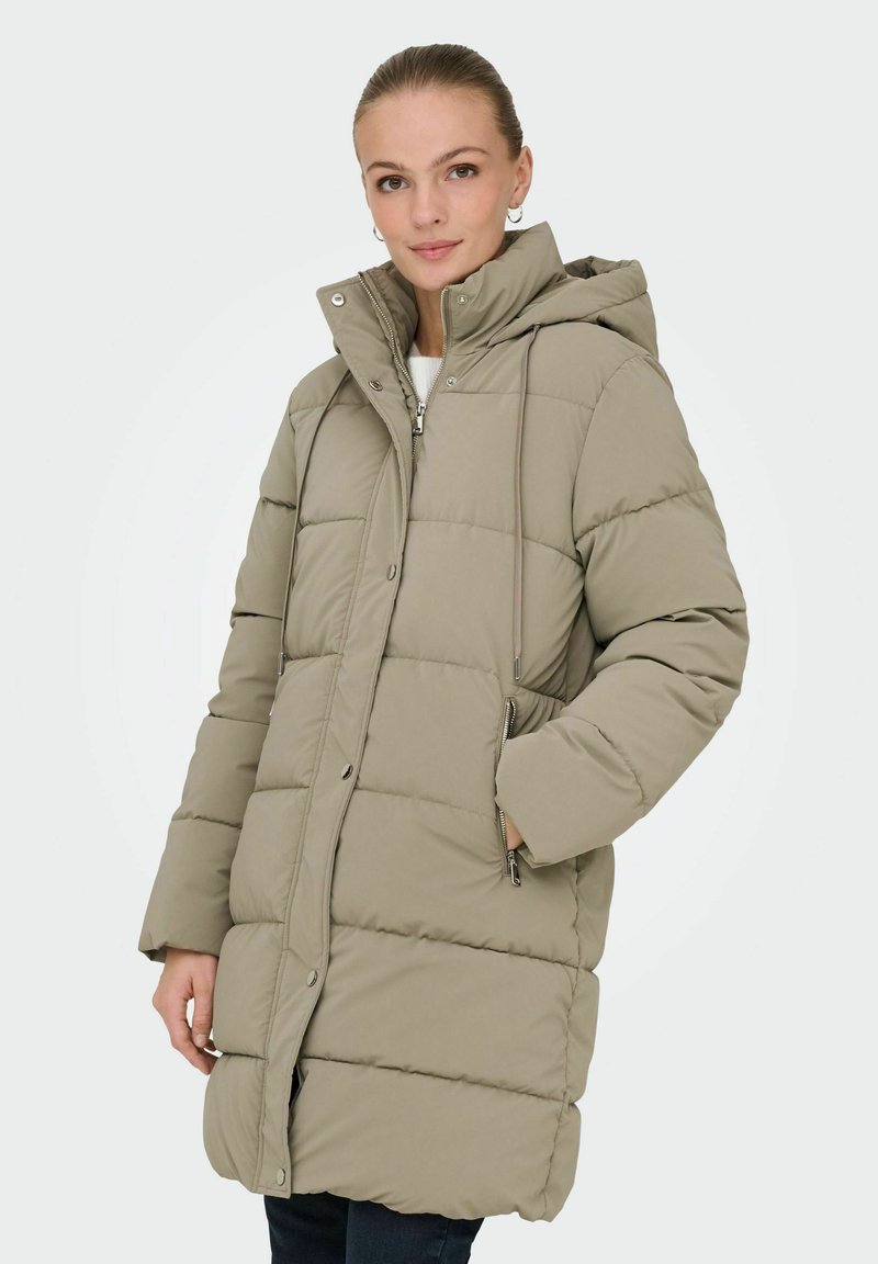 Beige polstret parka med hætte, der har lynlåslukning foran, sidelommer og quiltet tekstur. Mellemlang model for varme.
