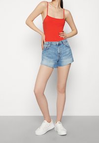 Röd ärmlös bodysuit ihop med ljusblå denimshorts. Shortsen har fransade kanter och hög midja. Vita sneakers med f ärgglada detaljer fulländar looken.