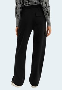 Black cargo pants with wide legs, featuring two side pockets and a back pocket, made from a soft, textured fabric.