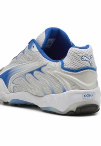 Chaussure de sport Puma blanche et bleue avec tissu en mesh, col matelassé et semelle épaisse avec logo de la technologie d’amorti CELL.