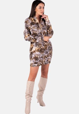 Langärmliges Kleid mit einem abstrakten Muster in Braun, Grau und Creme, das einen Reißverschlusskragen hat. Dazu kombiniert mit beigen Stiefeln bis zum Knie.