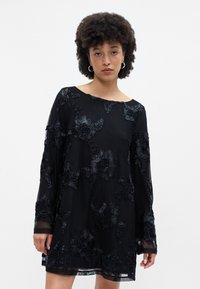 Melna kleita ar ziedu izšuvumiem, garām piedurknēm un laivas formas kakla izgriezumu. Caurspīdīgs audums ar teksturētu apdari, vidēja garuma apakšmalu.