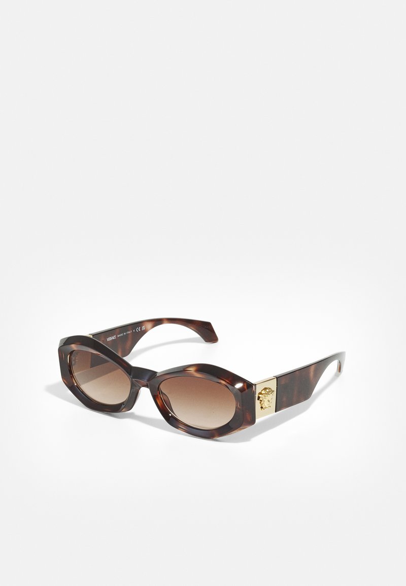 Sonnenbrille im Schildpatt-Look mit einer markanten achteckigen Form. Verborgene braune Gläser und eine goldene Akzentierung mit einem Löwenkopf am Bügel.