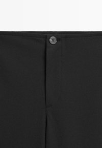 Pantalons noirs avec une fermeture à bouton à l'avant, une texture lisse et des coutures sur le taille et les coutures.