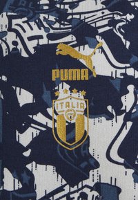 Tela de marca Puma con un patrón abstracto en azul marino y blanco, con un diseño de logotipo dorado y escudo para Italia, enfatizando la textura y el color.
