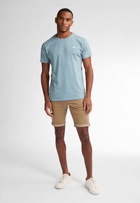 Lyseblå t-shirt med rund hals og struktureret stof, kombineret med beige shorts med oprollende kanter og beige sneakers.