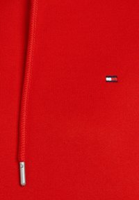 Sweatshirt rouge avec une finition texturée, doté d'un cordon en métal argenté et d'un petit logo brodé en bleu, blanc et rouge.