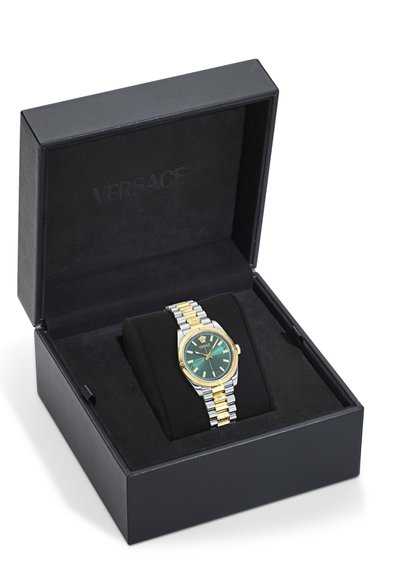 Versace laikrodis juodame dėžutėje su auksine ir sidabrine nerūdijančio plieno apyranke, žaliais ciferblatais ir auksiniu rėmeliu; eksponuojamas juodame paminkle su pagalvėlė.