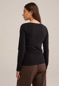 Schwarzes langärmliges, figurbetontes Oberteil mit weit geschnittenem Ausschnitt, glatter Textur und minimalistischem Design, kombiniert mit braunen hochgeschnittenen Hosen.