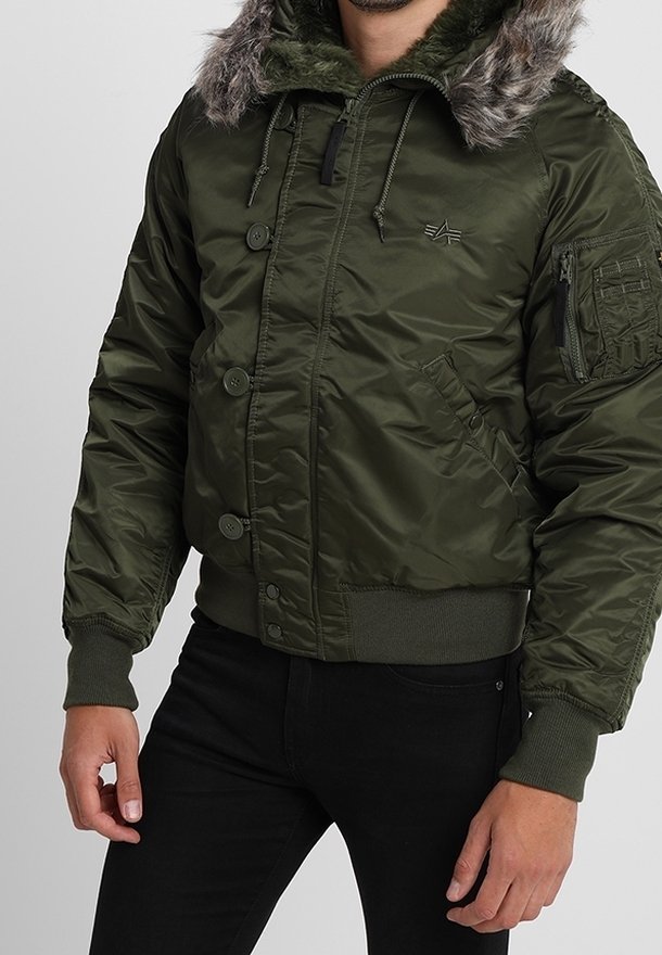 Grüne Bomberjacke mit Kunstfellkapuze, Reißverschluss- und Knopfverschluss, gerippten Bündchen und Saum, gesteppter Struktur und Utility-Tasche am Ärmel.