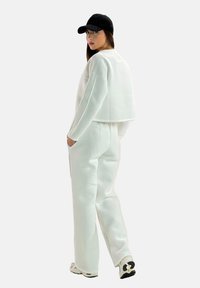 Witte cropped sweatshirt en bijpassende broek van zachte stof, met zijzakken, gecombineerd met een zwarte pet en witte sneakers.