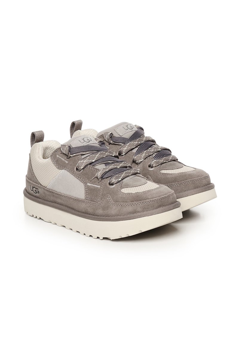 Zapatillas de ante gris con detalle de panel de malla, suela de goma y cordones texturizados. Presenta un logo en la lengüeta y en el lateral.